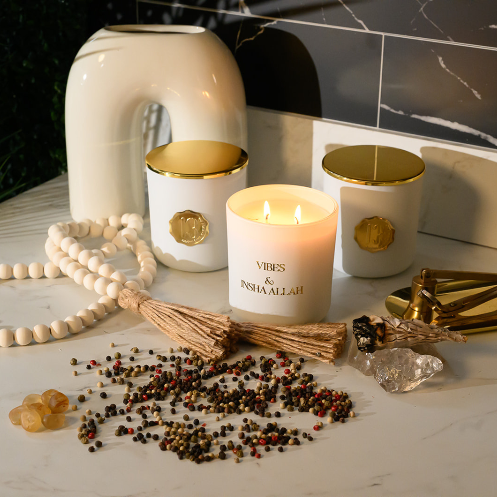 Handpoured white candle glass jar with a gold metal logo label, featuring multiple organic wicks, burning with a warm glow. The candle is made with natural coconut and soy wax and non toxic fragrance oils. Decorative candle for aesthetic appeal