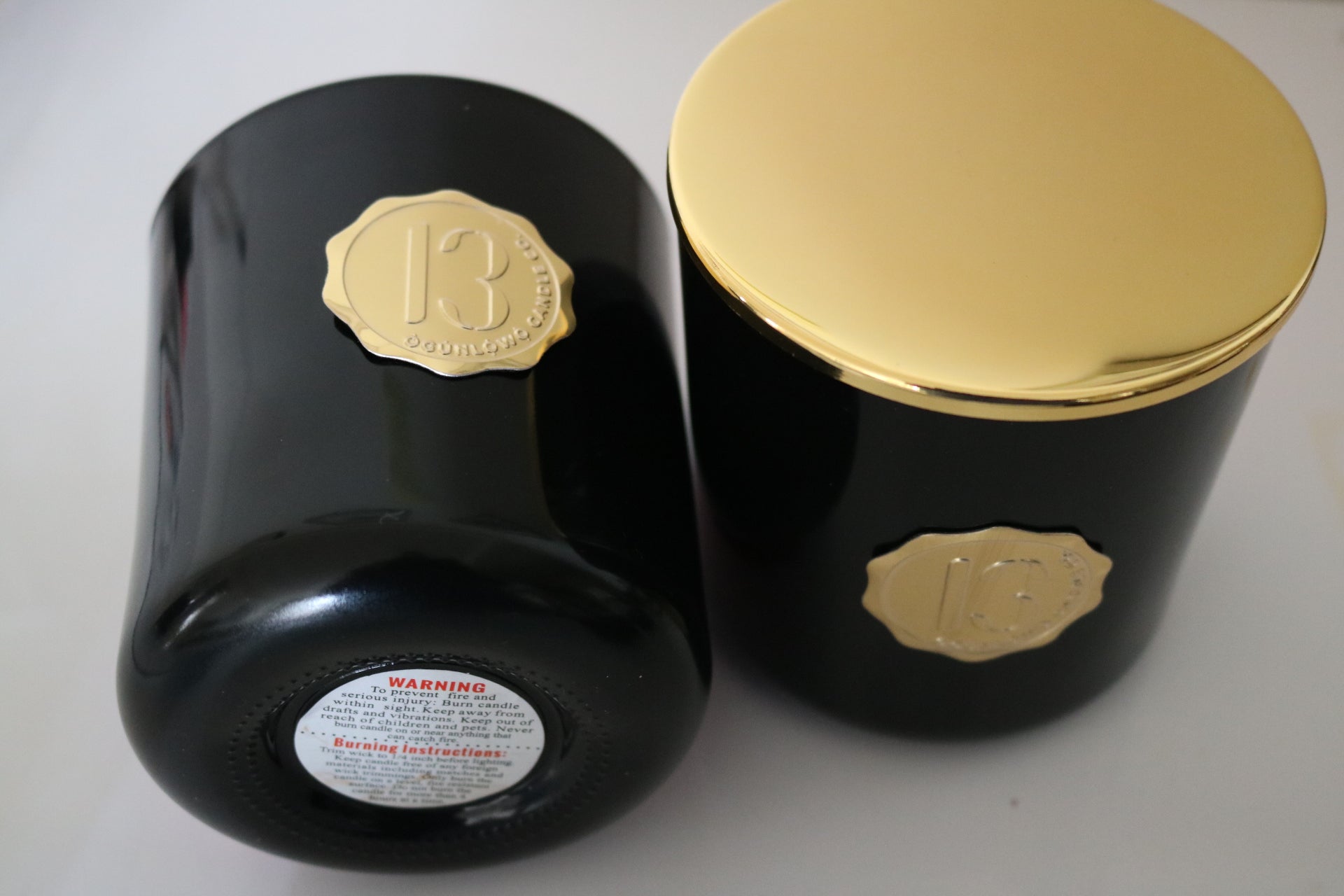 A black candle glass jar with a gold lid and label, featuring multiple organic wicks, burning with a warm glow. The candle is made with natural coconut and soy wax and non toxic fragrance oils
