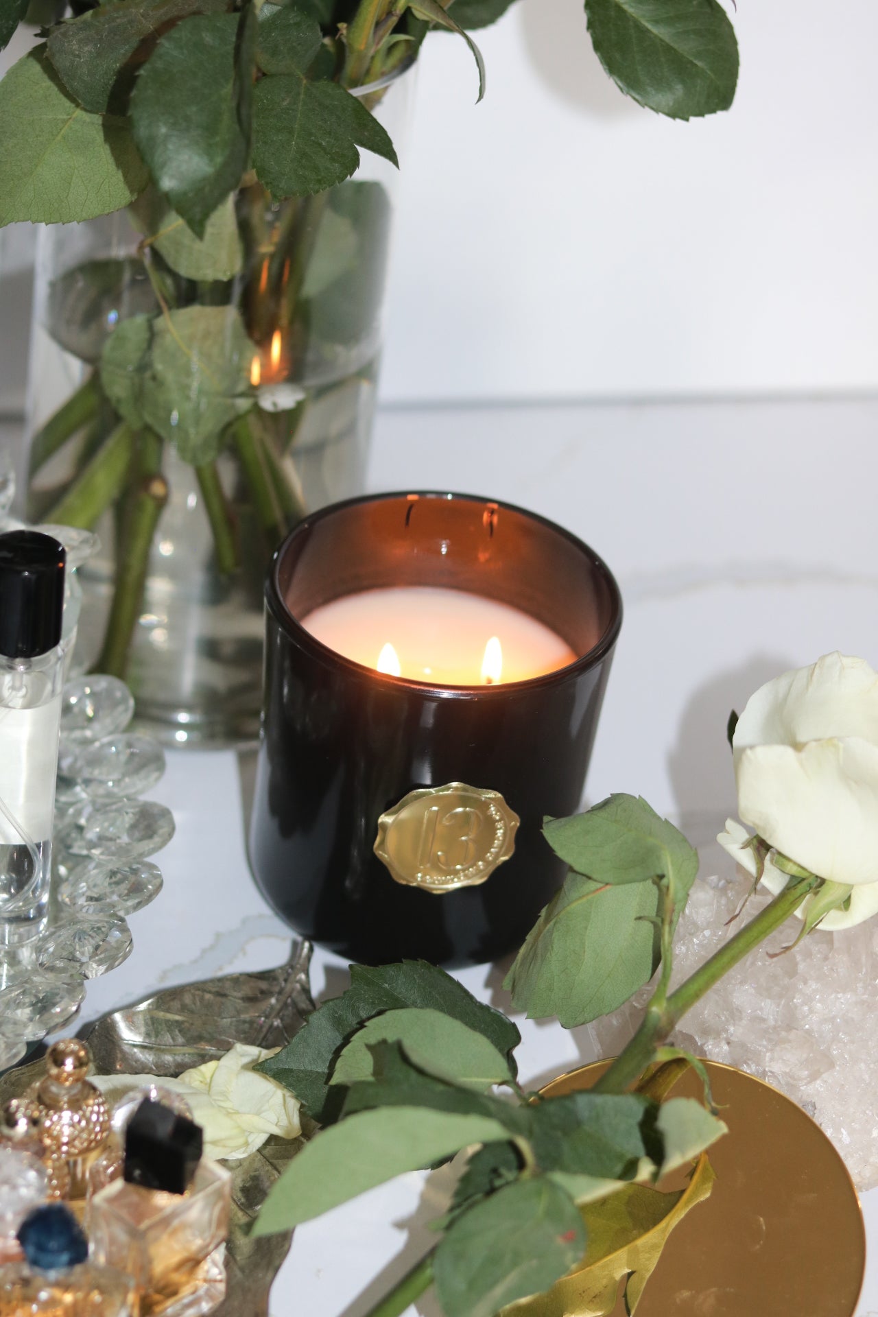 A black candle glass jar with a gold metallic label, featuring multiple organic wicks, burning with a warm glow. The candle is made with natural coconut and soy wax and non toxic fragrance oils. Decorative candle for aesthetic appeal