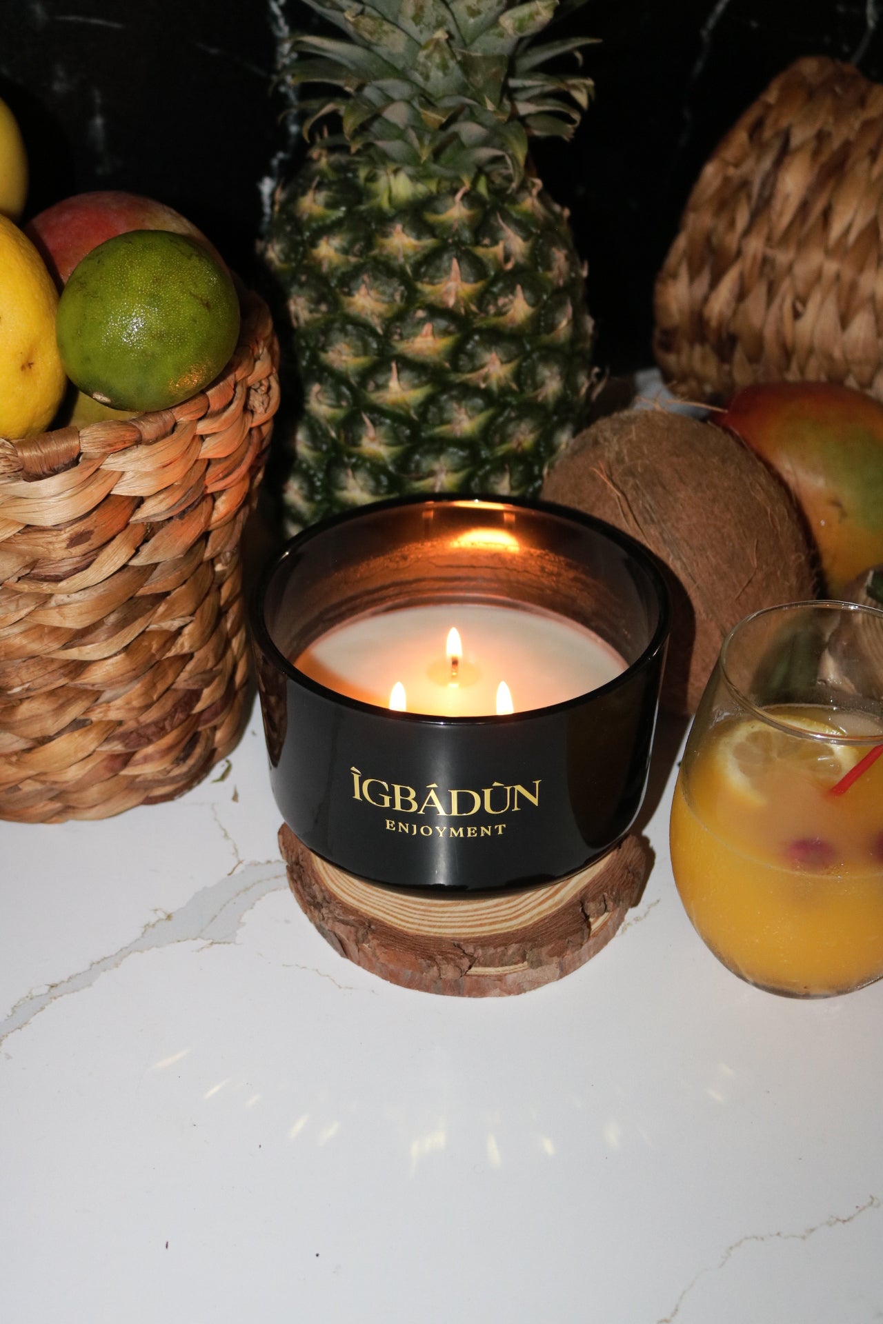 A black bowl candle with a gold label, featuring multiple organic wicks, burning with a warm glow. The candle is made with natural coconut and soy wax and non toxic fragrance oils