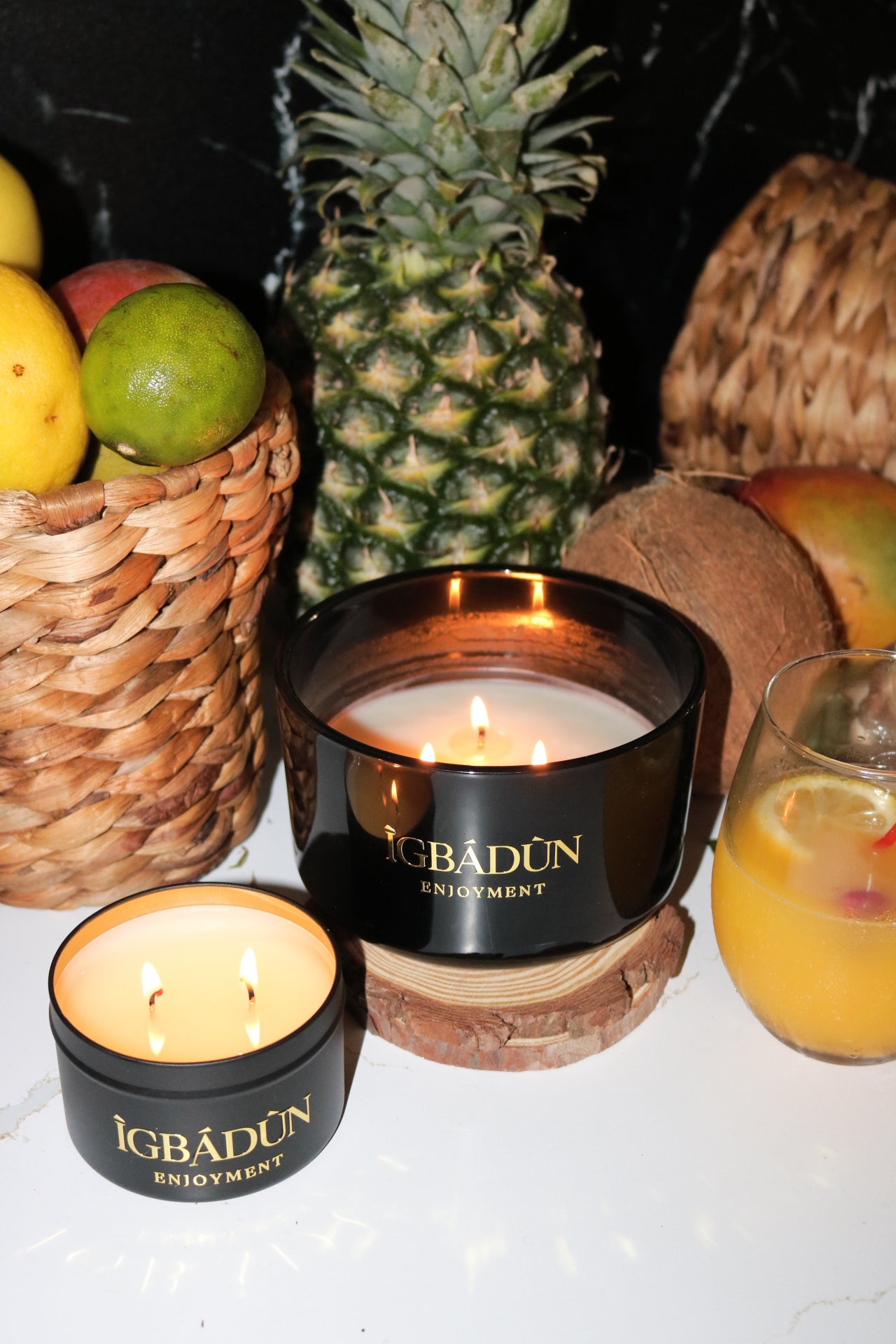A black bowl candle with a gold label, featuring multiple organic wicks, burning with a warm glow. The candle is made with natural coconut and soy wax and non toxic fragrance oils