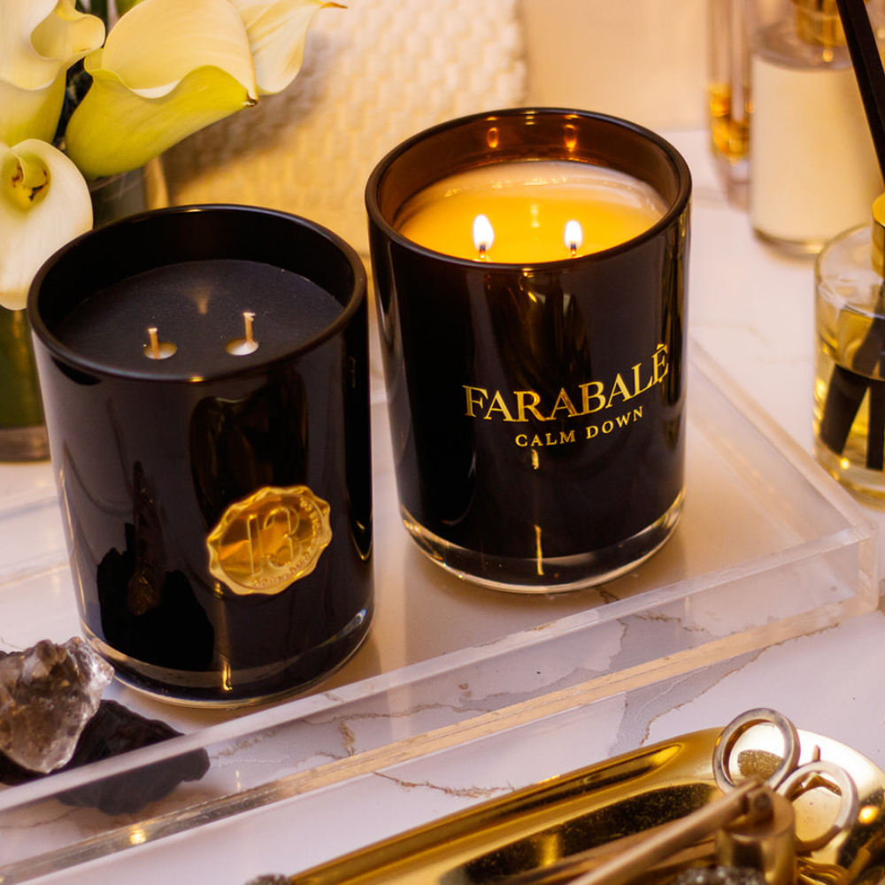 A black candle glass jar with a gold lid and label, featuring multiple organic wicks, burning with a warm glow. The candle is made with natural coconut and soy wax and non toxic fragrance oils