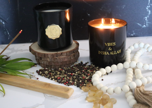 A black candle Jar with a gold label, featuring multiple organic wicks, burning with a warm glow. The candle is made with natural coconut and soy wax and non toxic fragrance oils