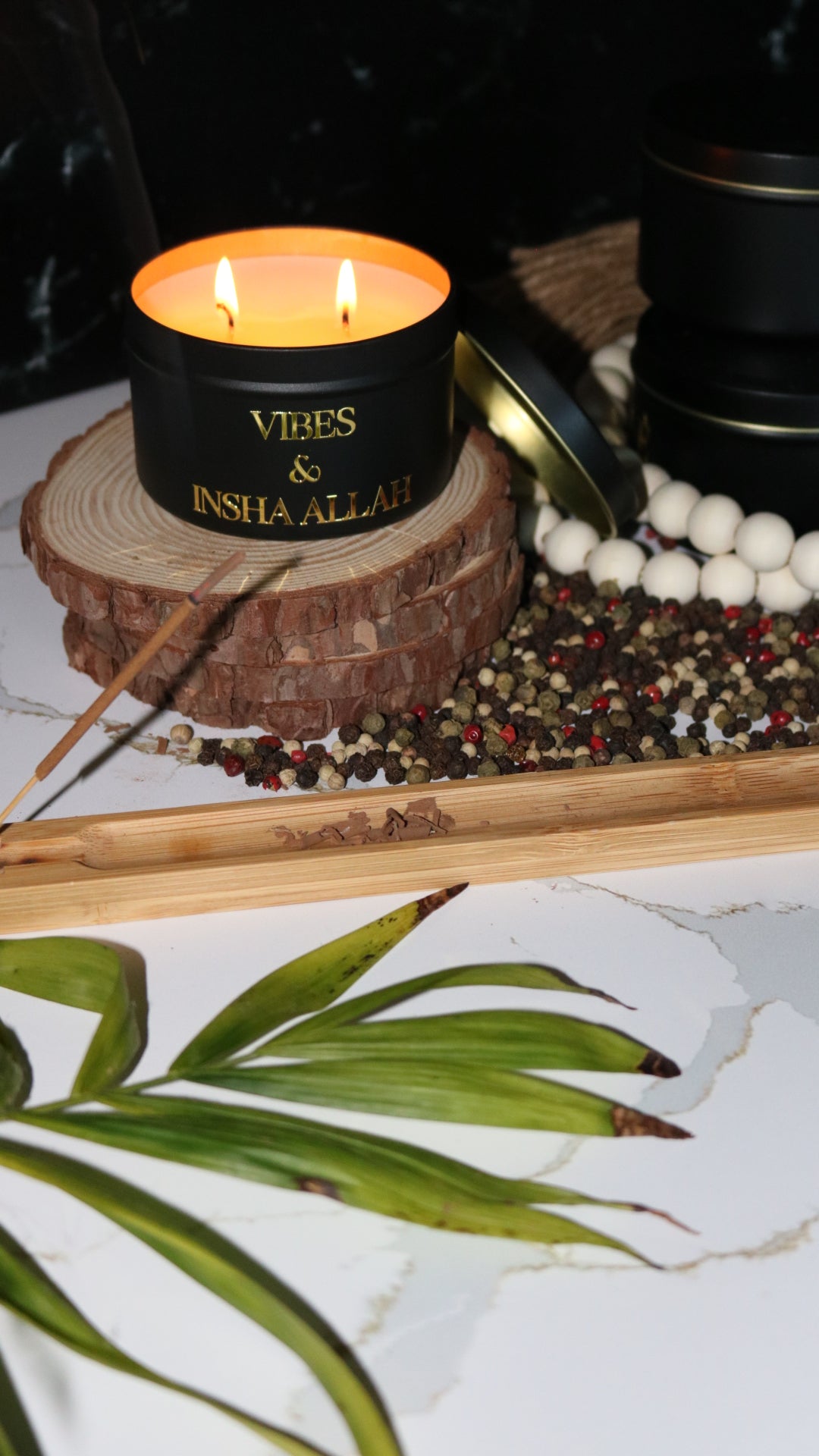 A black candle metal tin with a gold metal logo label, featuring multiple organic wicks, burning with a warm glow. The candle is made with natural coconut and soy wax and non toxic fragrance oils. Decorative candle for aesthetic appeal