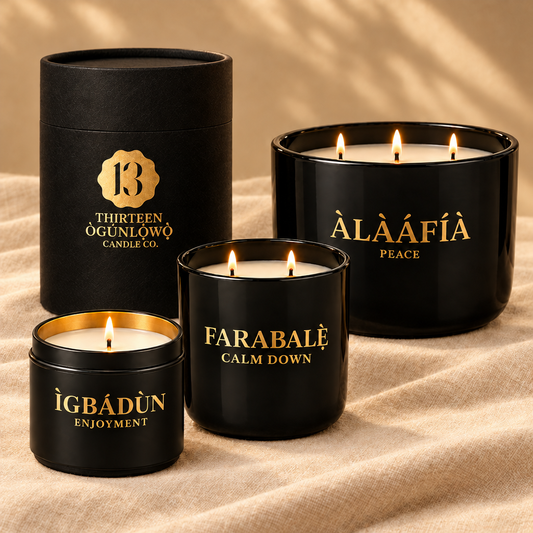 Three 13 Ògúnlọ́wọ̀ candles in black and gold, a 6oz Ìgbádùn tin, a 12oz Farabalẹ̀ tumbler with gift tube, and a 15oz Àlàáfíà three-wick bowl, on cream linen