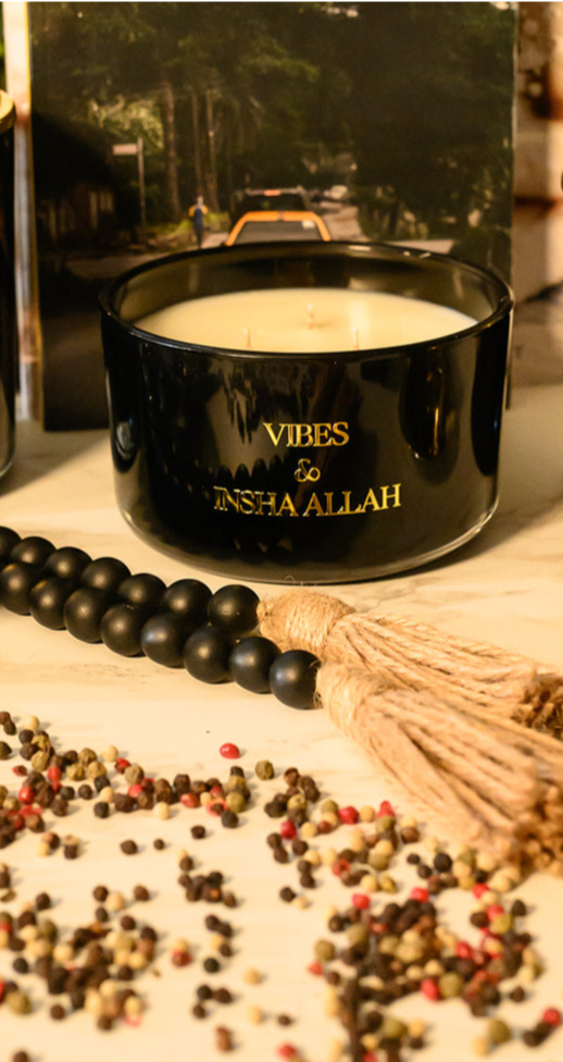 Hand poured black glass candle container with a gold metal logo label, featuring multiple organic wicks, burning with a warm glow. The candle is made with natural coconut and soy wax and non toxic fragrance oils. Decorative candle for aesthetic appeal