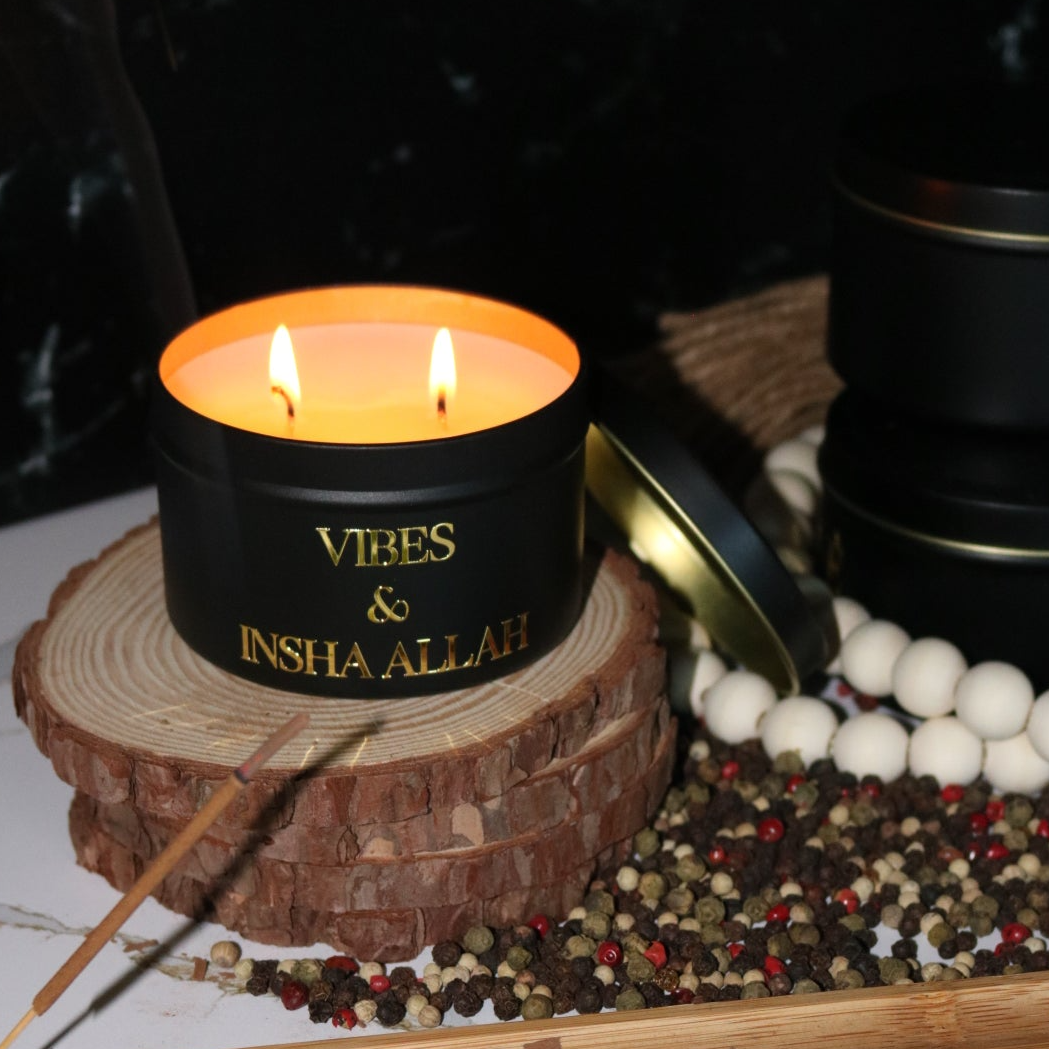 Hand poured black candle tin with a gold metal logo label, featuring multiple organic wicks, burning with a warm glow. The candle is made with natural coconut and soy wax and non toxic fragrance oils. Decorative candle for aesthetic appeal
